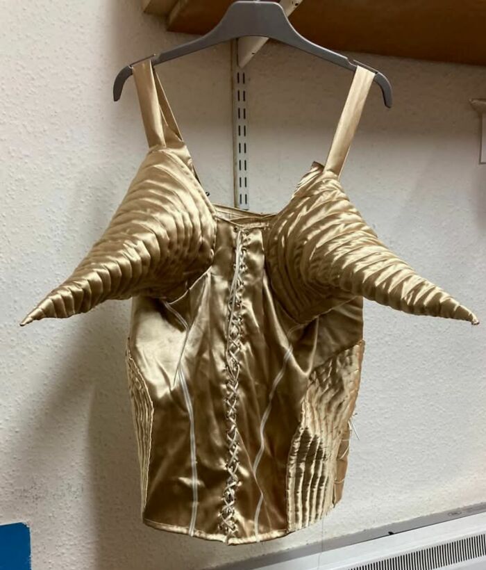 Unusual cone-shaped gold corset hanging on a shop hanger, a bizarre treasure from a secondhand store.