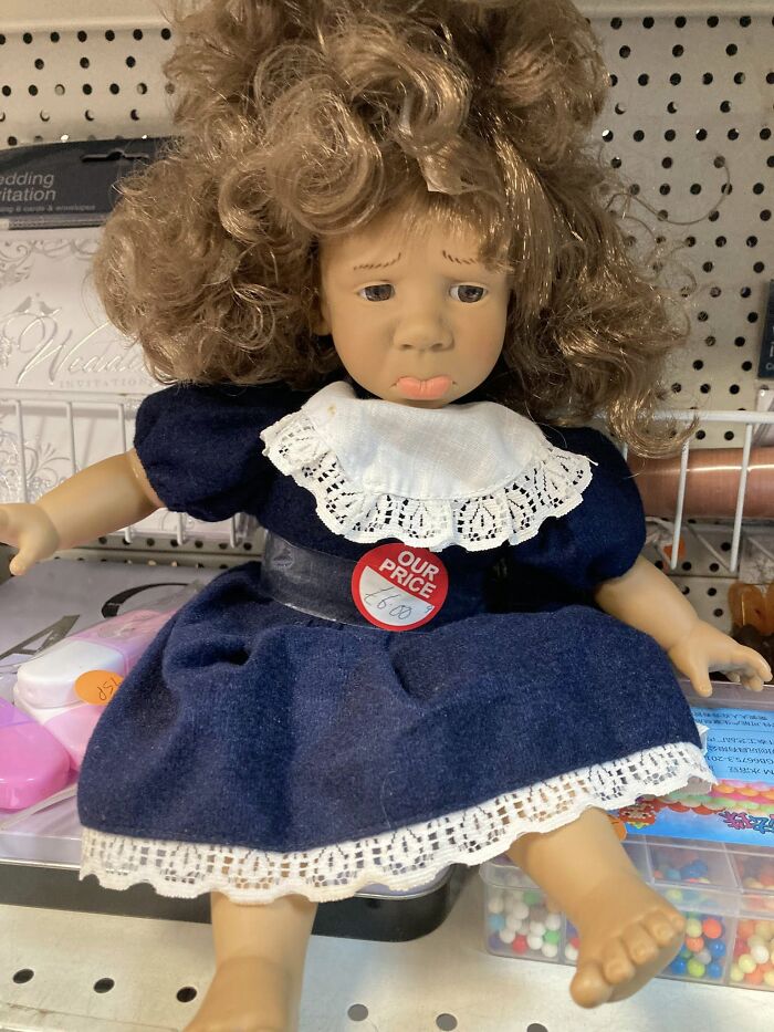Sad-faced doll in a blue dress with a price tag, found in a secondhand shop.