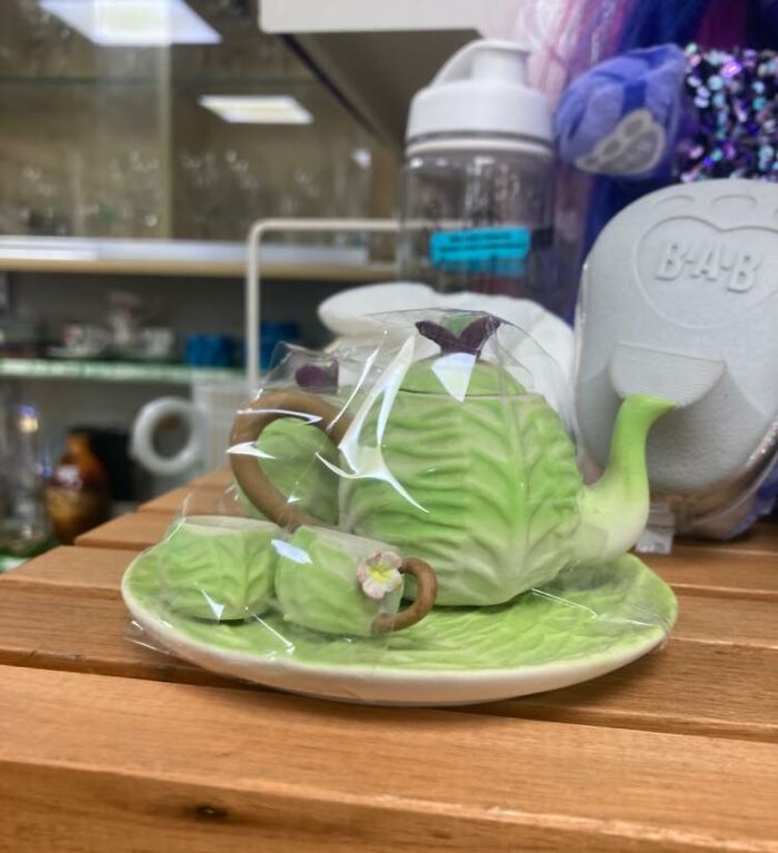 Cabbage-shaped teapot set wrapped in plastic on a wooden shelf in a secondhand shop.