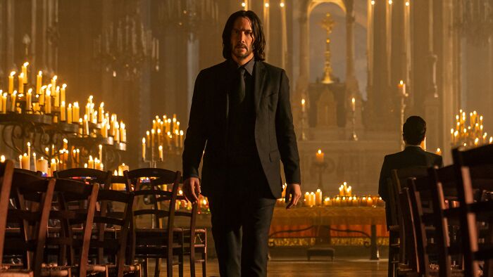 Man in a black suit walks through a candlelit hall, emitting a mysterious and dramatic aura.