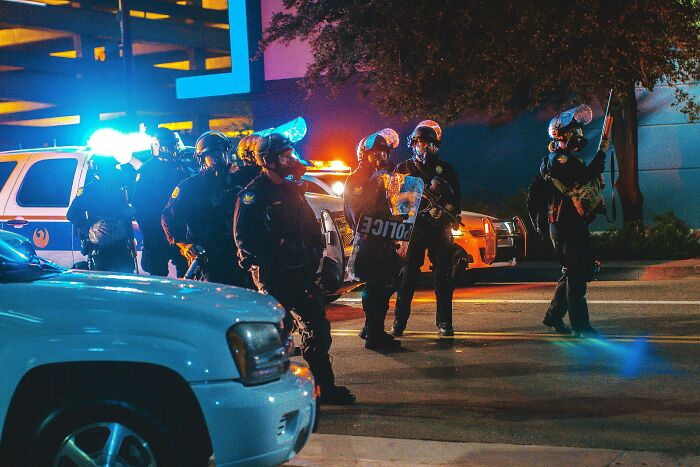 Police officers in riot gear at night with patrol cars and flashing lights, providing a fascinating scene of law enforcement action.