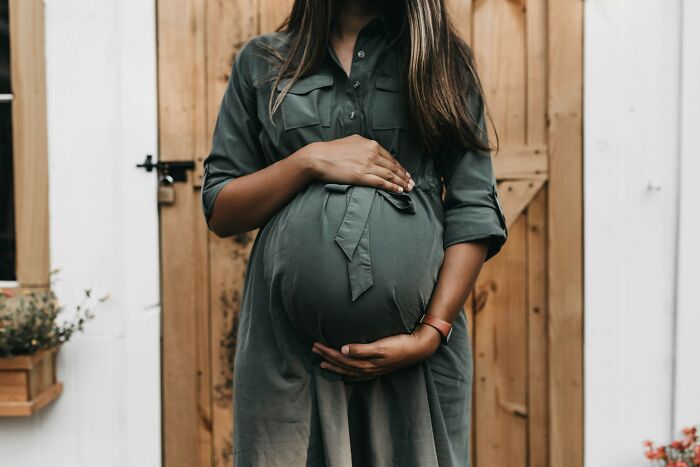 Pregnant woman in a green dress standing in front of a wooden door, gently holding her belly, random knowledge.