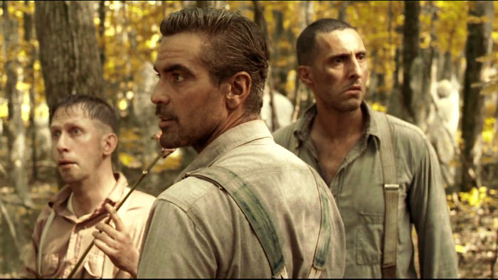Three men in vintage clothing stand in a forest, gazing intently in the same direction, adding to random knowledge intrigue.