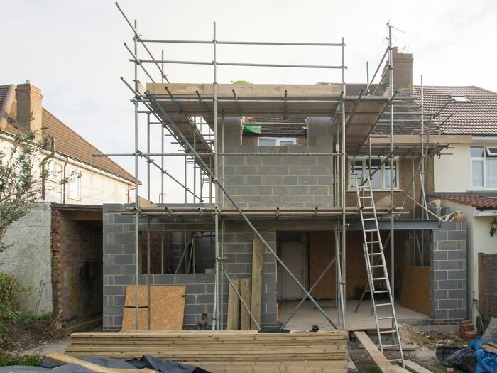 House under construction with grey bricks and scaffolding, showcasing random knowledge in building techniques.