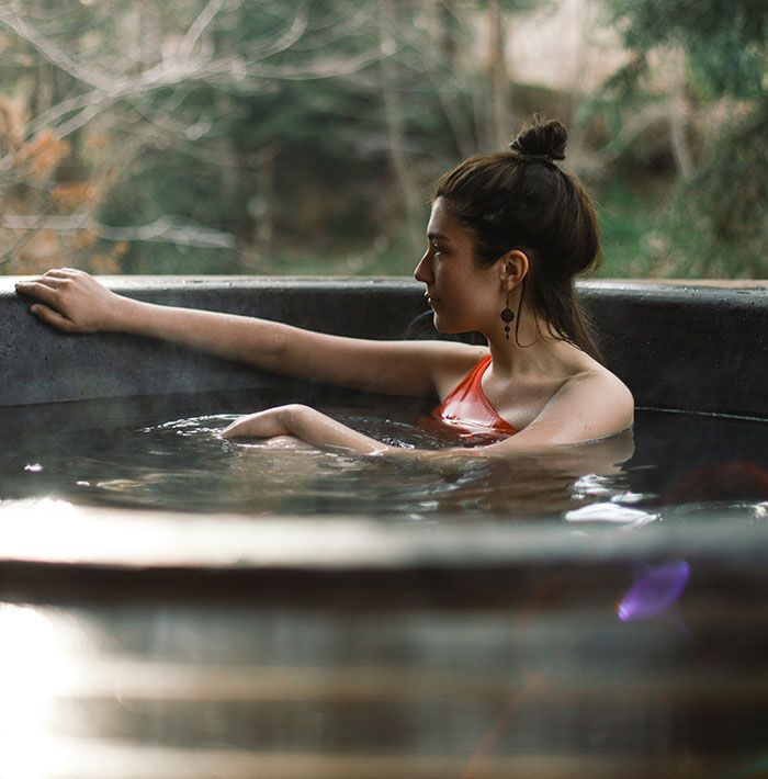 Woman in a red swimsuit relaxing in an outdoor hot tub, surrounded by nature.