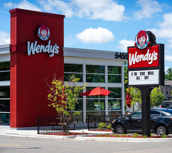 Wendy's restaurant exterior on a sunny day, featuring its sign and patio area. Wendy's restaurant exterior on a sunny day, featuring its sign and patio area.