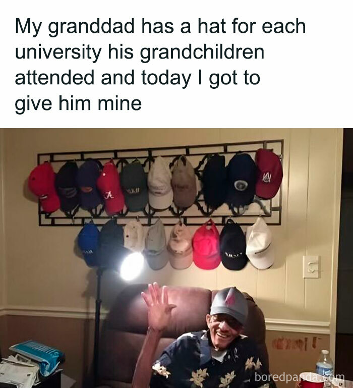 Elderly man waving happily in a chair, with a wall display of university hats, wholesome memes concept.