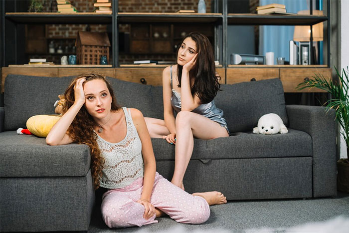 Two friends in pajamas sitting on a sofa, involved in an emotional discussion.