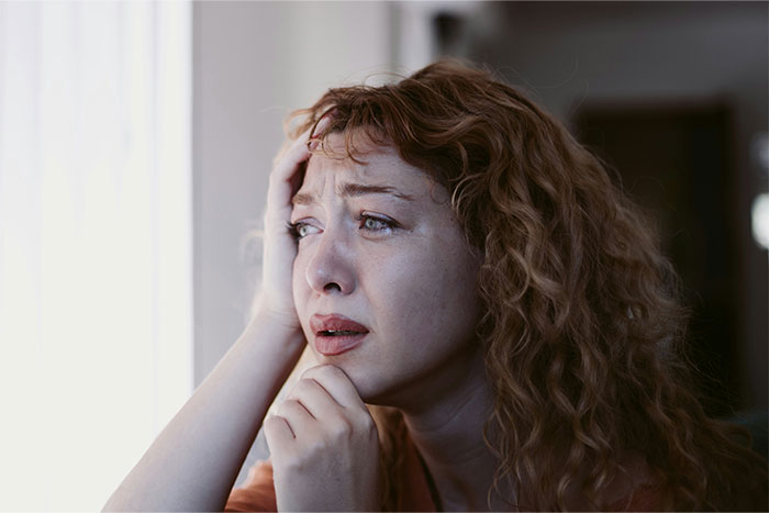A distressed woman with curly hair looks worried, touching her face, representing intense friendship-ending drama.