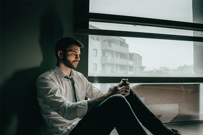 Man in a tie sitting by window, looking contemplative, sunlight casting shadow in friendship ending moment.