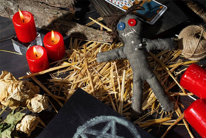 Voodoo doll with pins and candles on a bed of straw, possibly symbolizing tension in friendship-ending stories.