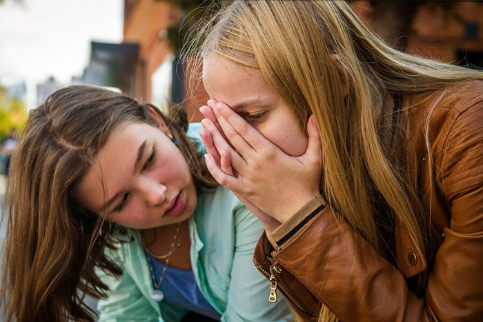 Two friends sharing a shocking secret outside, expressing disbelief and concern.