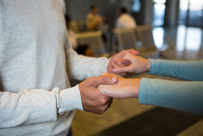 Two people holding hands in a waiting area, conveying support during a family visit. Two people holding hands in a waiting area, conveying support during a family visit.
