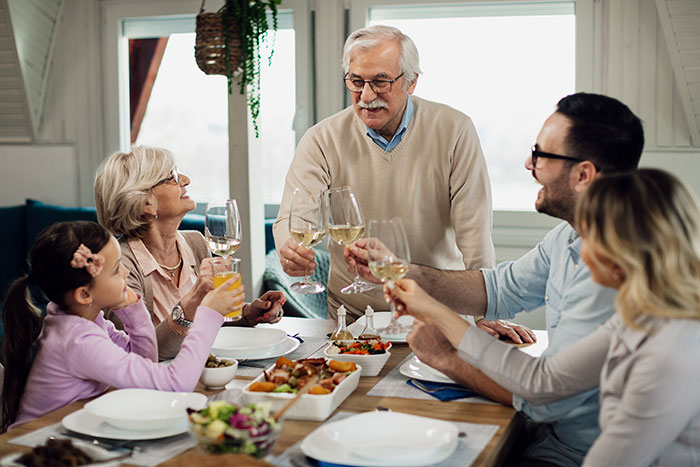 Family sharing a toast over dinner, featuring a mother-in-law visiting her son, enjoying a cheerful meal together. Family sharing a toast over dinner, featuring a mother-in-law visiting her son, enjoying a cheerful meal together.
