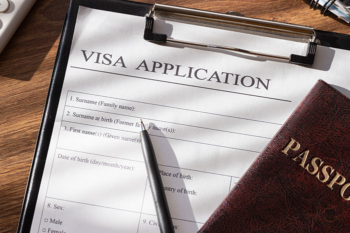 Visa application form and passport on a wooden desk, with a pen resting on the form under sunlight. Visa application form and passport on a wooden desk, with a pen resting on the form under sunlight.