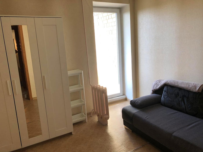 Small living room in a real estate property for sale featuring a black sofa, white wardrobe, and a window with natural light.