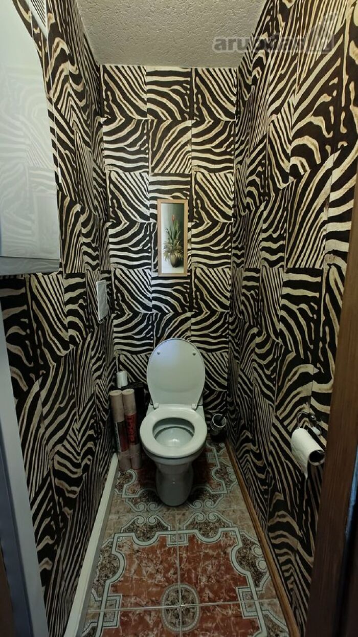 Small bathroom with white toilet and wild zebra print wallpaper, showcasing unique real estate property design features.
