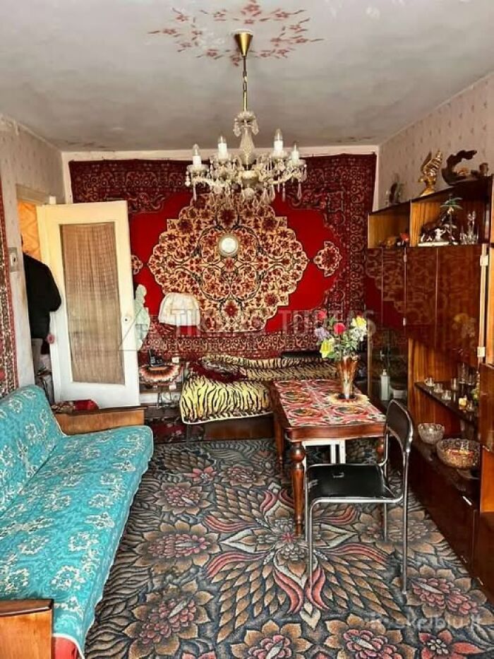 Eclectic real estate property interior with vintage furniture, patterned carpets, and ornate wall tapestry in a living room.