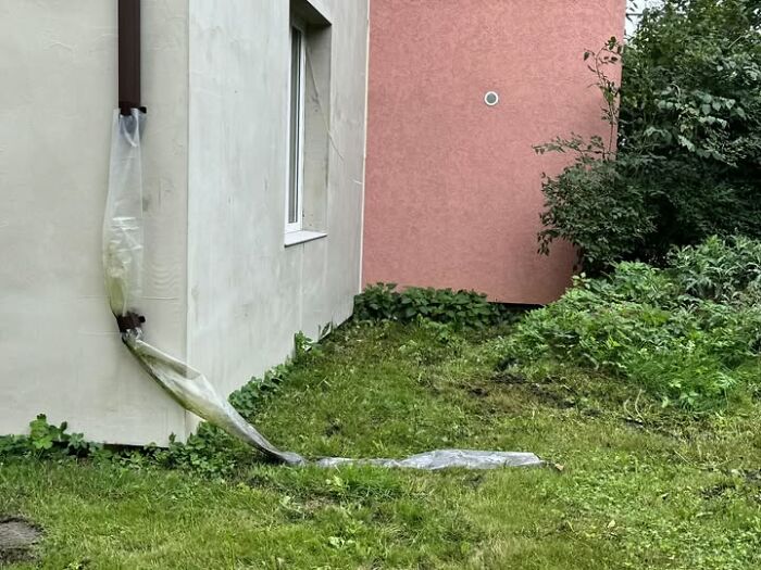 Unusual real estate property with a plastic wrapped downspout extending across a grassy yard near a pink and beige building.