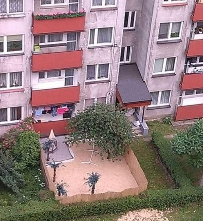Apartment building with a small enclosed sandy yard featuring fake palm trees, a unique real estate property for sale.