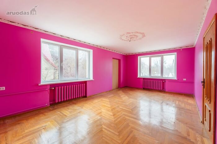 Bright pink walls in an empty real estate property with large windows and wooden parquet floors for sale listing.