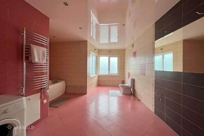 Spacious bathroom in a wild real estate property for sale with pink tiles, bathtub, toilet, and large windows.