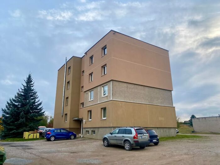 A multi-story wild real estate property with parked cars outside under a cloudy sky in a suburban area.