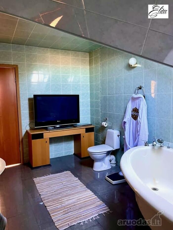 Bathroom with a bathtub, TV on a wooden desk, toilet, and tiled walls in a unique real estate property for sale.