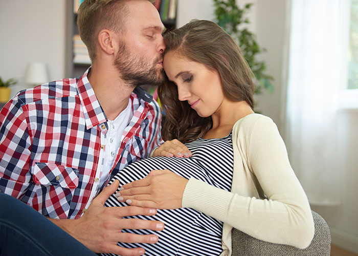 Pregnant woman and husband sharing tender moment, husband focused on her.