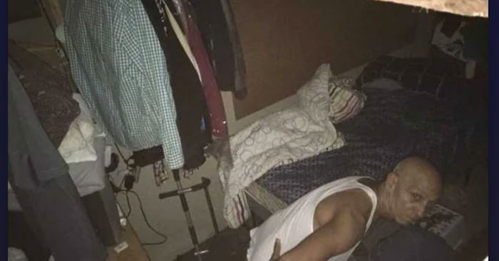 A man discovered crouching in a cluttered attic, surrounded by clothing and a bed. A man discovered crouching in a cluttered attic, surrounded by clothing and a bed.