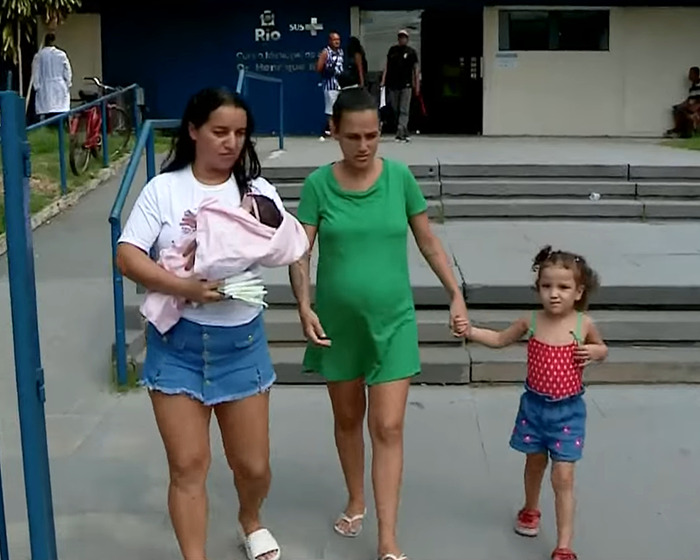 Pregnant woman with child and friend carrying baby outside hospital.