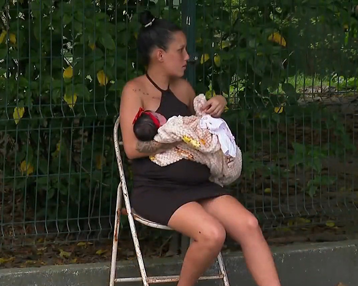 Pregnant woman holding one baby in her arms, sitting outdoors on a chair.