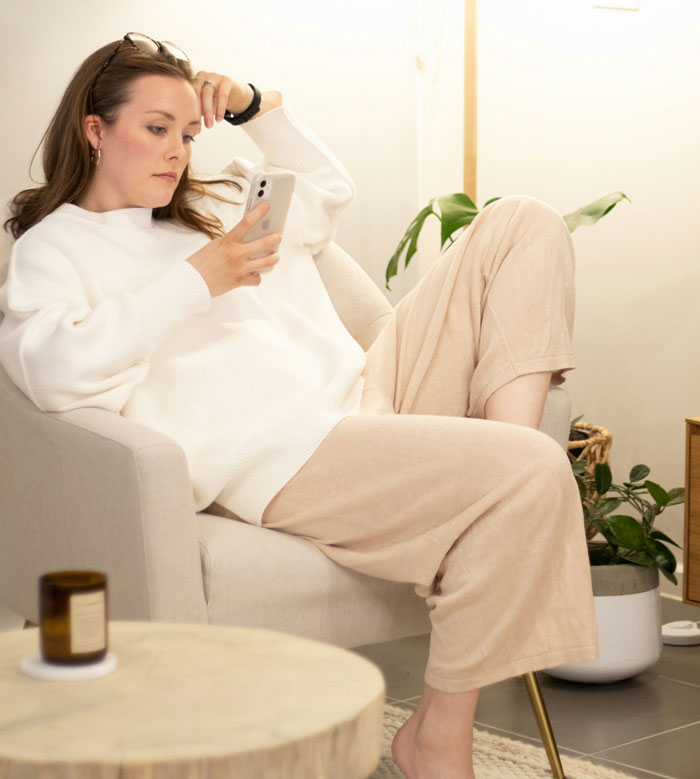 Woman relaxing in a chair, looking at her phone, with a thoughtful expression about visiting siblings, nieces, and nephews.
