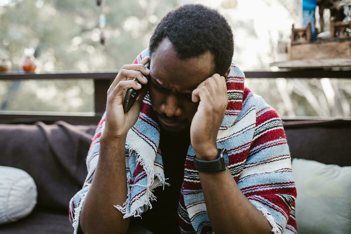 Man on phone, wrapped in a colorful blanket, looks stressed about sister-in-law and caravan situation.