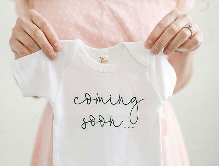 Person holding a baby onesie with "coming soon," relating to name change secrecy.