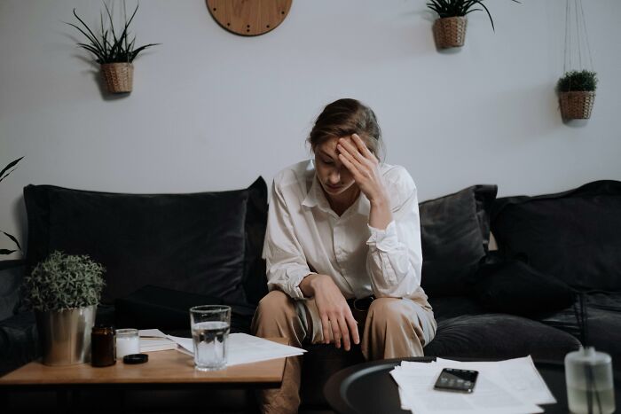 Woman looking stressed, sitting on a couch with papers and a phone, related to parenting and weekend challenges with toddlers.