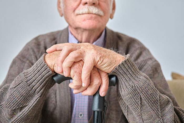 Elderly man with a cane, wearing a cardigan and sitting, representing family dynamics and complex father-daughter relationship.
