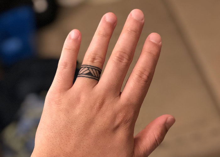 A hand with a geometric tattoo resembling a ring on the ring finger.