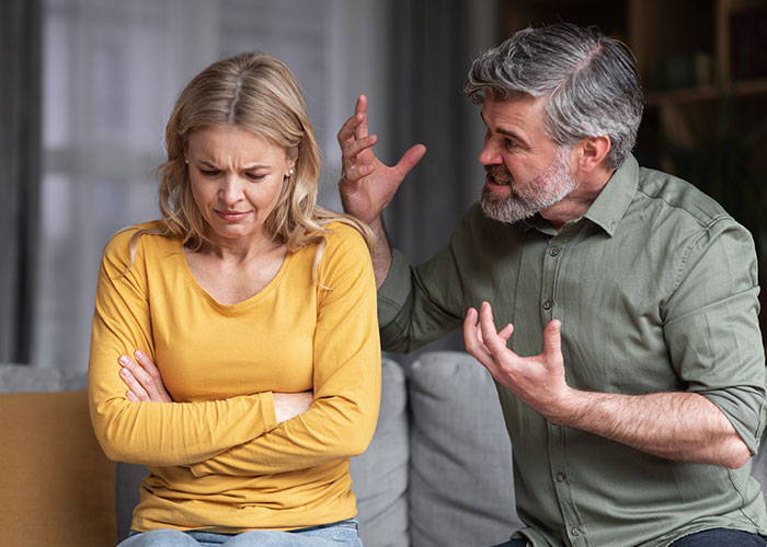 Man upset future wife keeps tattoo from late husband, sitting on couch in discussion.