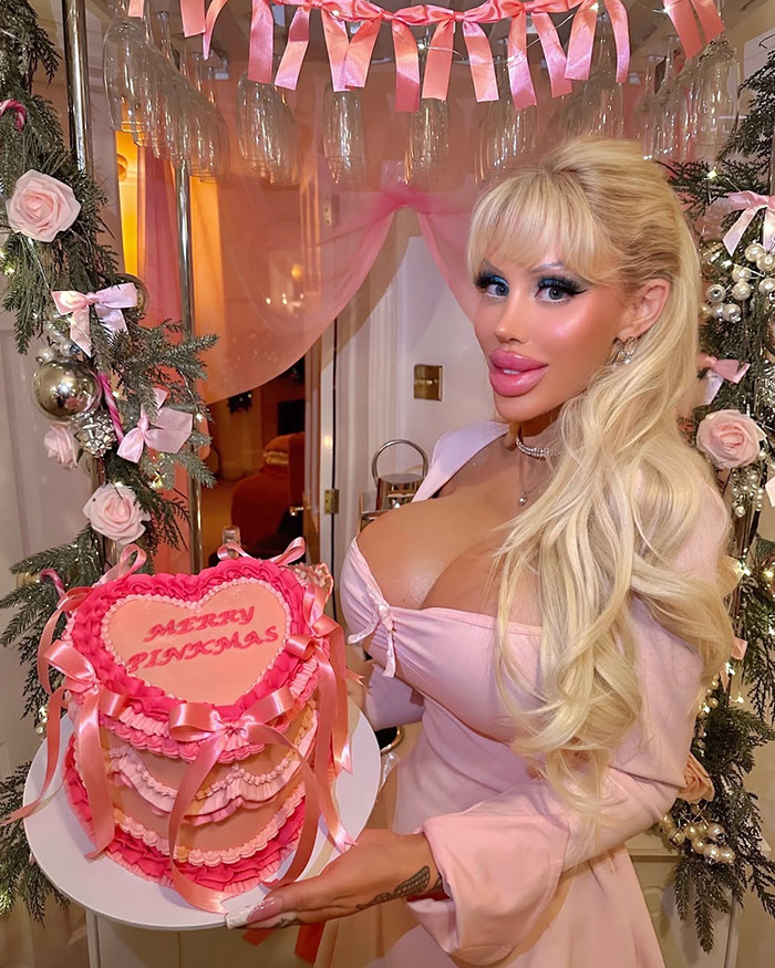Barbie-inspired woman holding a pink, decorated cake at a festive event.