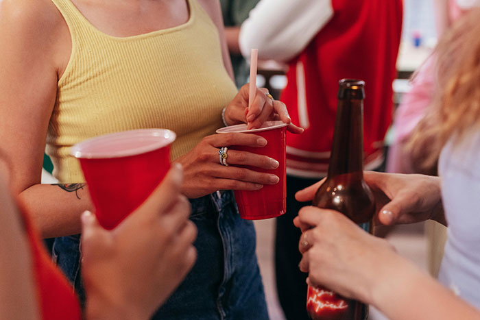 People at a party holding red cups and a beer bottle, engaging in conversation while socializing.