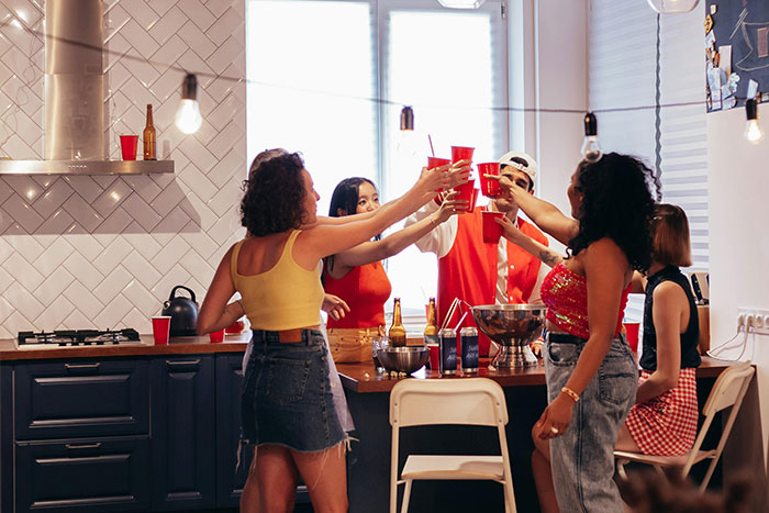 Friends celebrating in a kitchen, holding red cups and smiling, with festive decorations in the background.