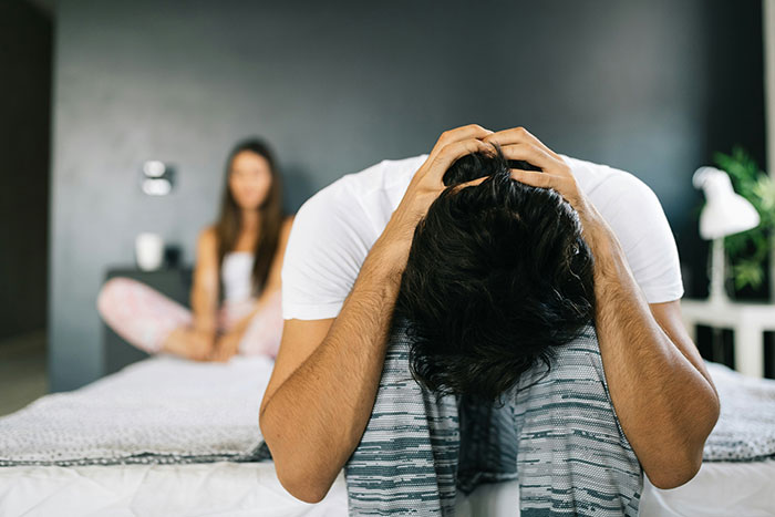 Man with head in hands, upset, while woman sits in background; celebrating disagreement at birthday dinner.