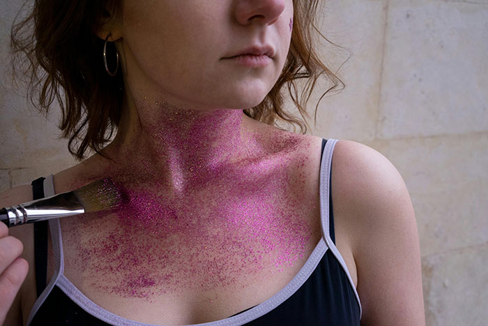 Woman applying pink glitter on her neck and shoulders as deterrent against men. Woman applying pink glitter on her neck and shoulders as deterrent against men.