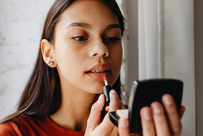 Woman applying lipstick using a compact mirror, exploring glitter as deterrent from men. Woman applying lipstick using a compact mirror, exploring glitter as deterrent from men.