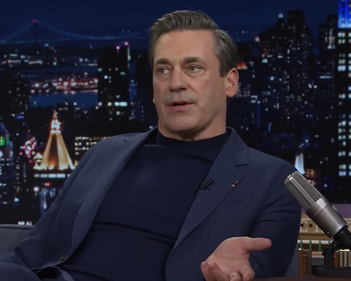 Actor discusses past incident on a talk show, wearing a blue suit with a cityscape backdrop.