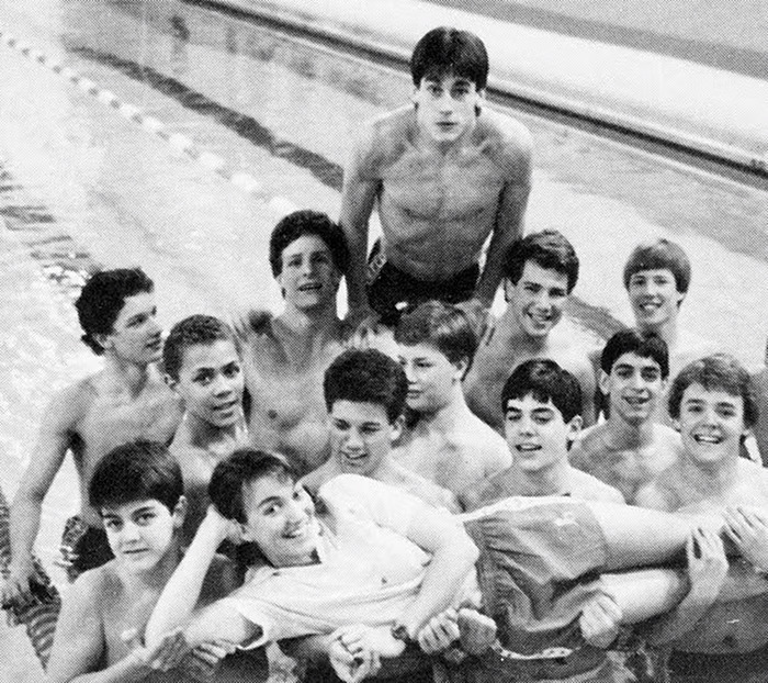 Group of young men at a university swimming pool, smiling and posing together.