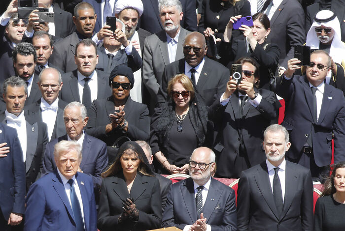 World leaders at a gathering, people capturing the moment on phones, highlighting potential disrespect at an official event. World leaders at a gathering, people capturing the moment on phones, highlighting potential disrespect at an official event.