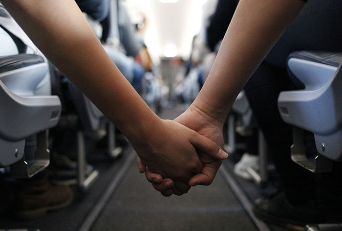 Passengers holding hands across a plane aisle, illustrating challenging seatmate experiences.
