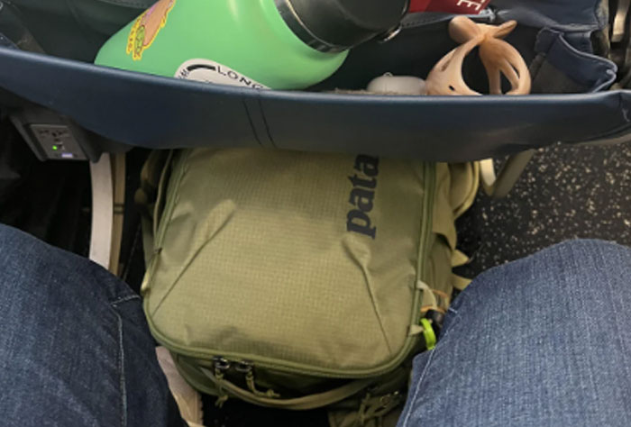 Passenger's cramped legroom with backpack and water bottle under plane seat, illustrating bad plane seatmate experience.